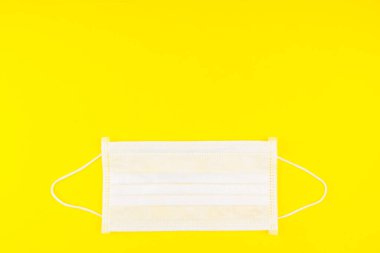 Cerrahi Yüz Maskesi sarı arka planda izole edilmiş. Coronavirus Konsepti. Virüsün yayılmasını durdurmak için tıbbi yüz maskesi. Plastik kulaklıklı cerrahi maske. Ağız burnu için cerrahi maske..