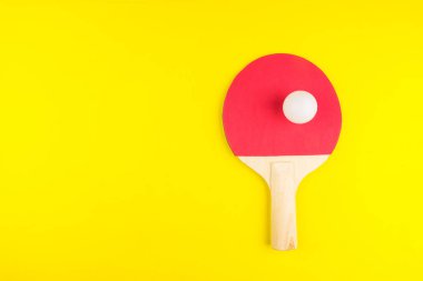 Sarı arka planda topu olan masa tenisi raketi. Spor kavramı..