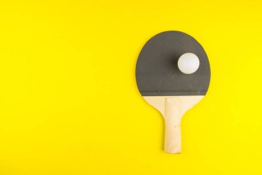 Sarı arka planda topu olan masa tenisi raketi. Spor kavramı..