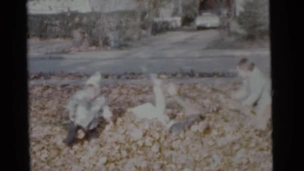 Niños jugando en la pila de hojas de otoño — Vídeo de stock