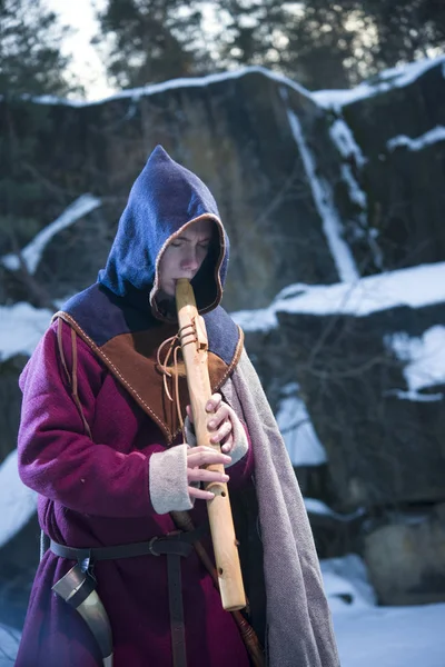 Guy in a medieval costume with a hood playing on a pipe, in the winter — Stock Photo, Image