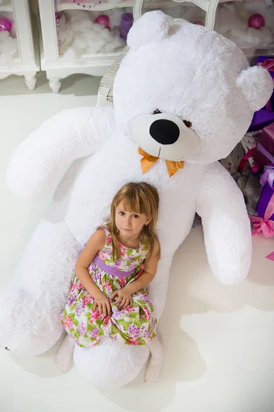 A menina está sentada num urso de peluche branco no Natal. Um brinquedo é um presente de Natal . — Fotografia de Stock