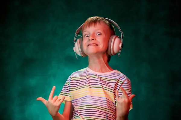 Kleine jongen luistert naar zijn favoriete rockmuziek in moderne draadloze hoofdtelefoon, in de studio — Stockfoto