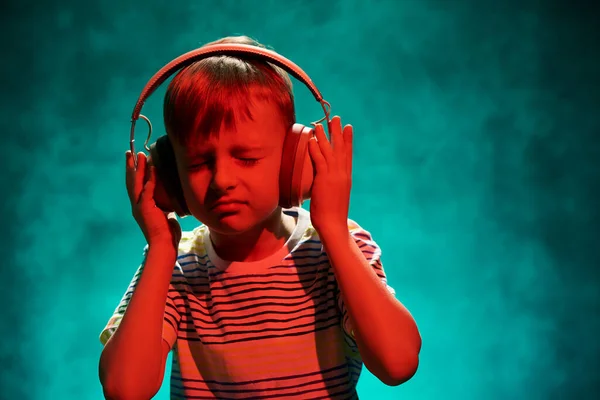 Мальчик слушает свою любимую музыку в современных беспроводных наушниках, в студии — стоковое фото
