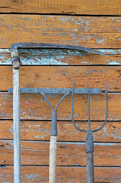 Pitchfork, scythe, hark op de achtergrond van de oude houten bruine muur — Stockfoto