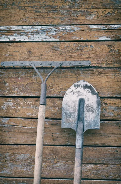 Pala sucia y un rastrillo en la pared de madera pintada de fondo, tonificación retro — Foto de Stock