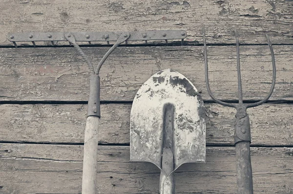 Spade, kratta och pitchfork mot väggen i bakgrunden målade trä, retro toning — Stockfoto