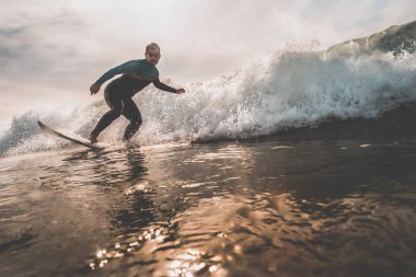 Genç adam bir dalga günbatımında sörf