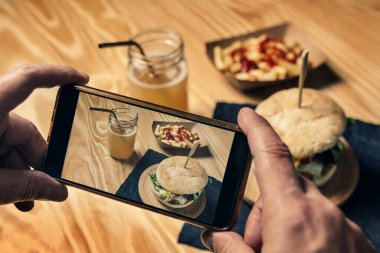 Erkek eli, telefonuyla hamburger fotoğrafı çekiyor.