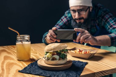 Şef hamburgerinin telefonuyla fotoğraf çekiyor.