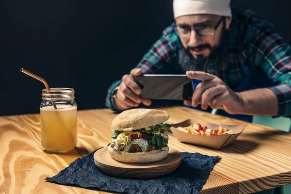 Şef hamburgerinin telefonuyla fotoğraf çekiyor.