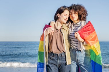 lesbian couple embracing wrapped in a rainbow flag