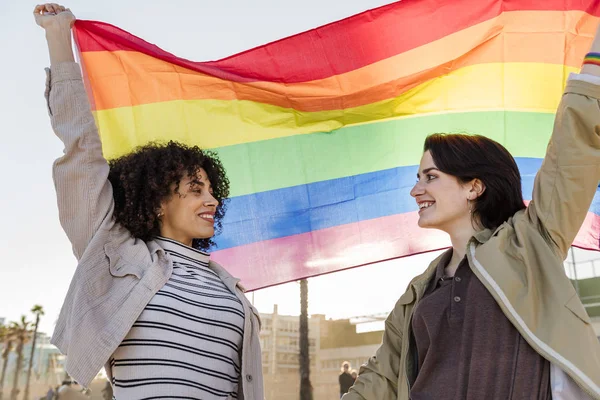 Coppia di ragazze sorridenti alzare la bandiera arcobaleno — Foto Stock