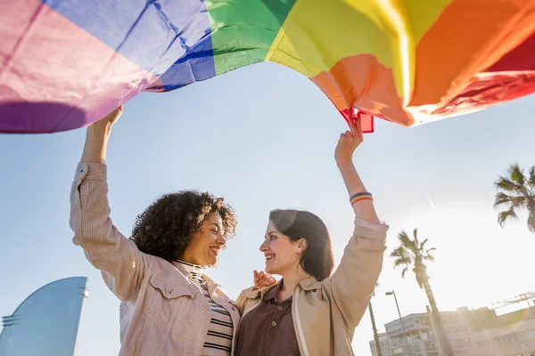 Smiling young lesbian couple waves a rainbow flag — Stok fotoğraf