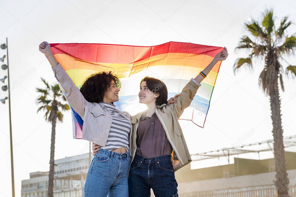 young lesbian couple smiling under a rainbow flag
