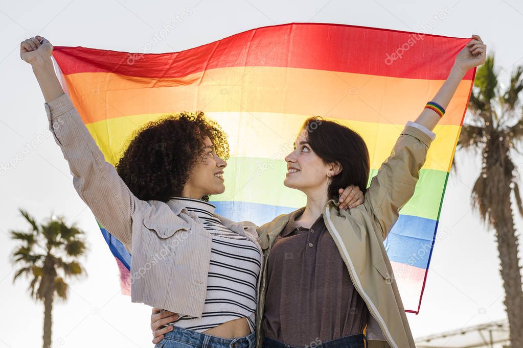 young lesbian girls hugging and waving a gay flag