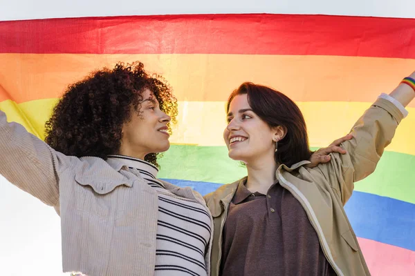 Mladé lesbičky pár objetí pod duhou vlajku — Stock fotografie