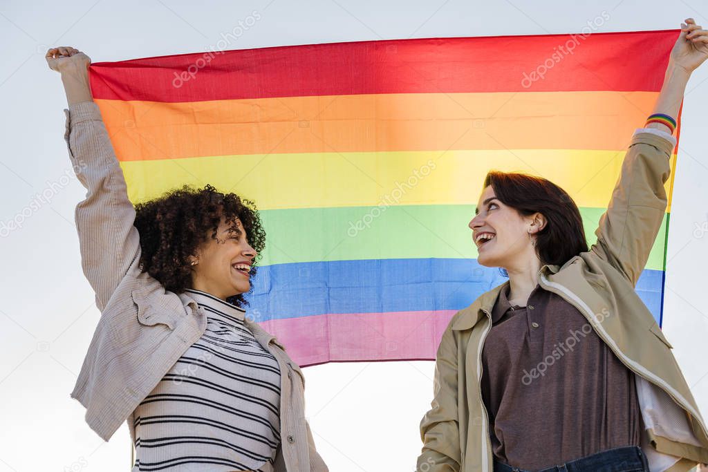 couple of smiling women raising the rainbow flag