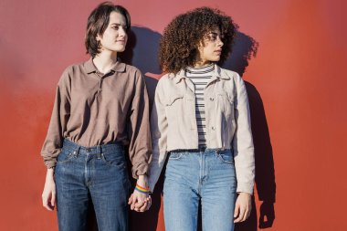 Kırmızı arka planda el ele tutuşan lezbiyen çift