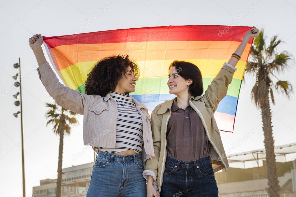 multiracial lesbian couple raising a rainbow flag