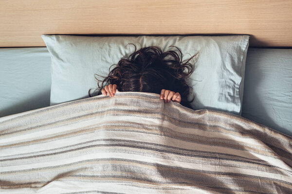 little joker girl covering her face with a bedspread, happy childhood and healthy rest concept