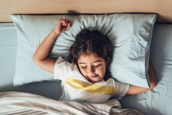 Sabah uyandığında yatakta uzanan küçük bir kızın üst görüntüsü. Mutlu çocukluk ve sağlıklı dinlenme kavramı.
