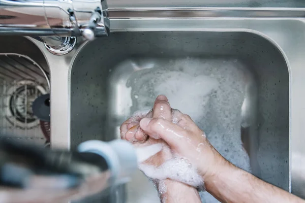 top view of two hands of a man taking off the soap with water in a metallic pile with soap foam, virus prevention, hygiene and skin care concept