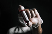 tmavá fotografie lékaře s ochrannými rukavicemi a lékařskou maskou zobrazující injekční lahvičku se vzorkem krve infikovaným kovid-19, koncept koronavirového výzkumu, selektivní zaměření na injekční lahvičku