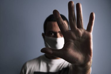 Koruyucu maskeli bir adamın portresi elinde mavi arka planda dur işareti, seçici odaklanma, koronavirüs konsepti ve virüslere ve bakterilere karşı koruma