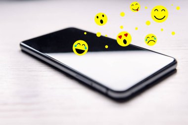 Beyaz ahşap masadaki bir telefondan gelen emojiler, sosyal medya ve iletişim konsepti, metin için kopyalama alanı, seçici odaklanma