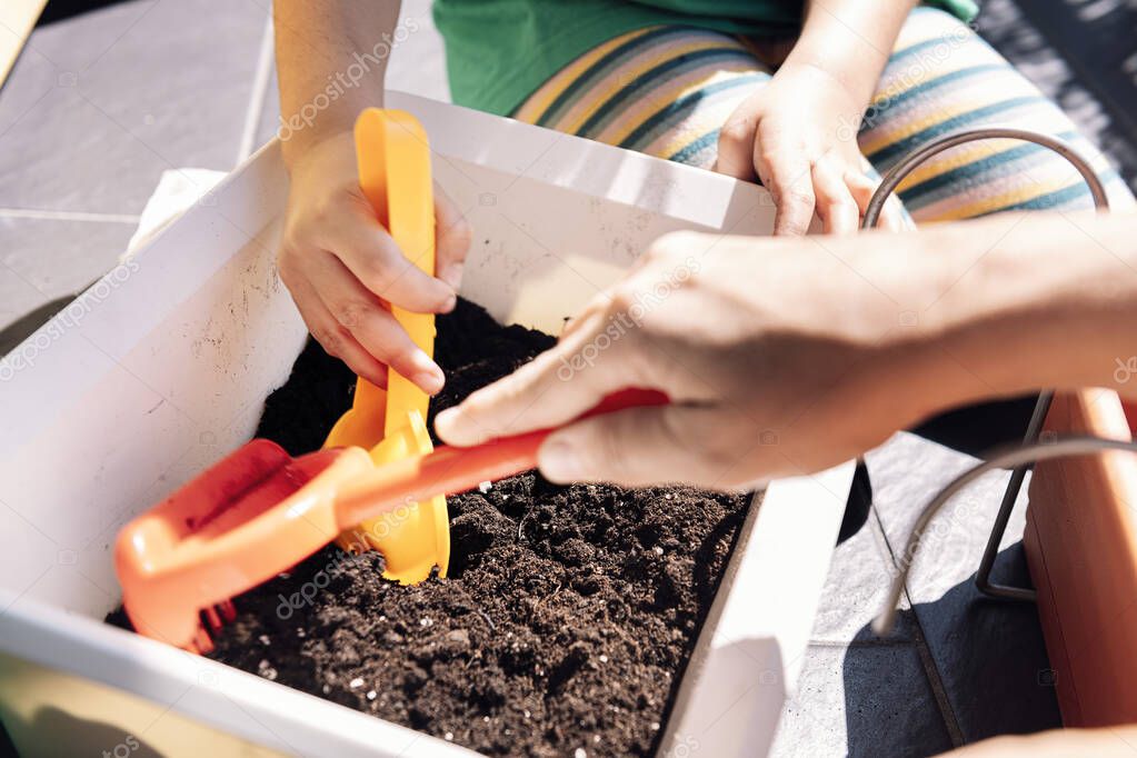 hands of a child and her mother in the balcony preparing gardening sand in pots for planting seeds, hobbies at home, sustainable and ecological lifestyle concept