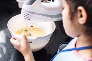 Yemek tarifi hazırlamak için mutfakta mikser kullanan küçük bir kız. Çocuklarla evde boş vakit geçirme kavramı.