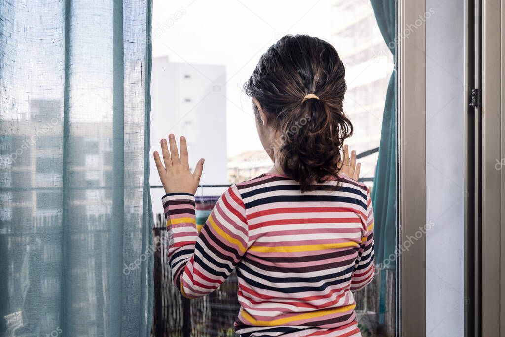 back view of an unrecognizable little girl looking through the window pane of home, concept of children in quarantine