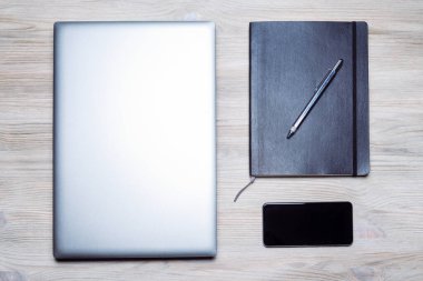 Minimalist düz dizüstü bilgisayar, akıllı telefon, tahta masa üzerindeki defter ve kalem, online girişimci konsepti ve uzaktan çalışma