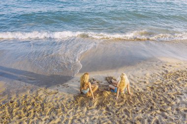Sahilde oturan iki sarışın kadın. Yaz mevsiminde dostluk ve rahatlama kavramı.