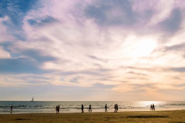 Yazın gün batımında sahilde yürüyen insanların silueti, yaz aylarında rahatlama kavramı.