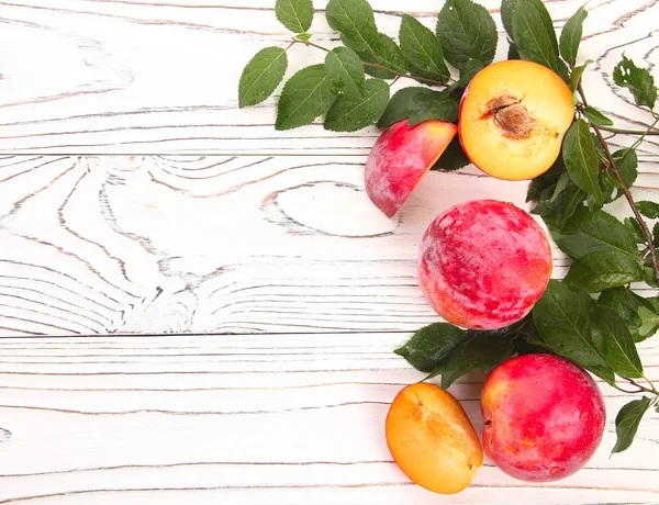 Röd frukt plommon med gröna blad på en trä bakgrund — Stockfoto