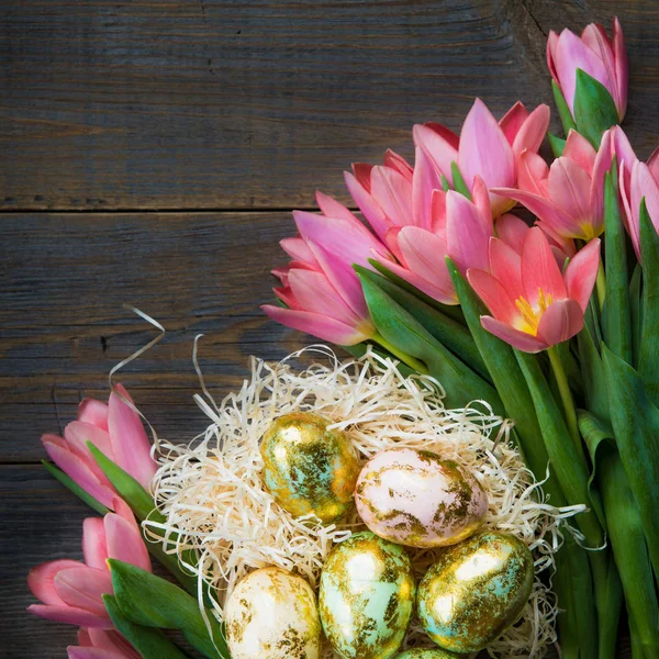 Zlaté velikonoční vajíčka a růžové tulipány Stock Obrázky