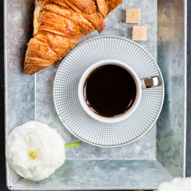 Taze kruvasan, fincan kahve ve tipik çiçekler. Kahvaltı