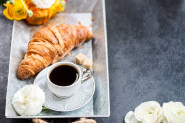 Taze kruvasan, fincan kahve ve tipik çiçekler. Kahvaltı