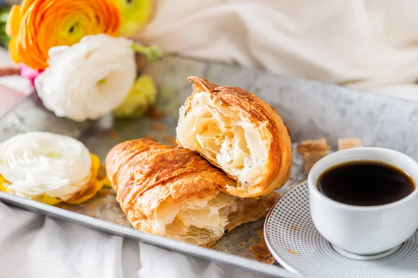 ครัวซองต์สด ถ้วยกาแฟ และดอกไม้แรนดิวคลัส อาหารเช้า — ภาพถ่ายสต็อก
