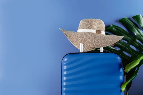 Maleta de tamaño cabina brillante y elegante con sombrero de paja y hoja de monstera —  Fotos de Stock