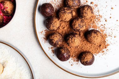 Hindistan cevizi ve limon, badem ve kakao, siyah çikolata ve fındık ezmeli gri tabak ve hafif arka plan gibi çeşitli ev yapımı çiğ vejetaryen mantarları veya enerji topları