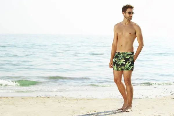 Hombre sin camisa de pie en la playa — Foto de Stock