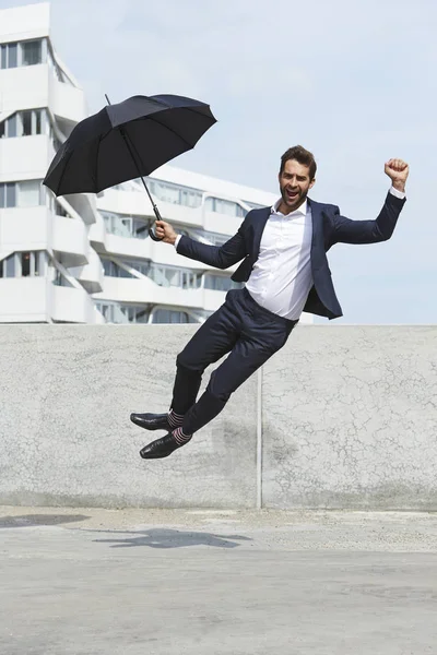 Businessman jumping with umbrella — Stock Photo, Image