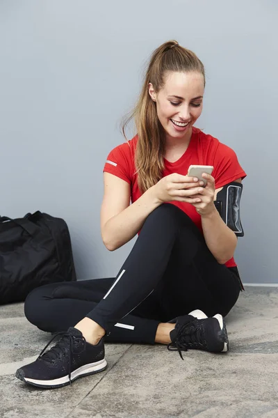 Lachende atletische vrouw met mobiele telefoon — Stockfoto