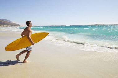 Kumsalda çalıştıran surfboard ile yakışıklı sörfçü