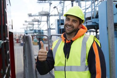 Yukarı başparmak ile gülümseyen liman işçisi