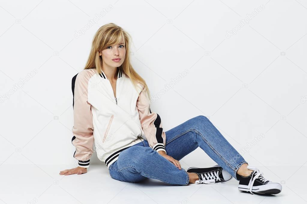 Beautiful girl in jacket and jeans sitting on floor looking at camera
