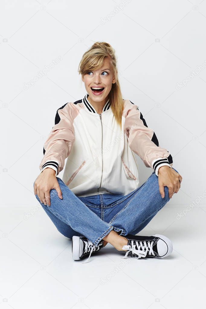 Excited girl in jacket and jeans sitting on floor